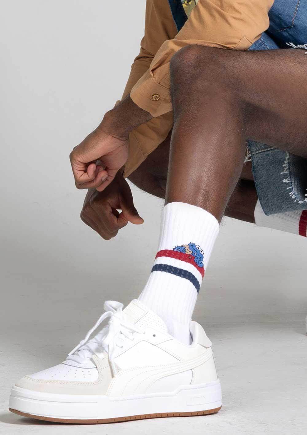 Imagen de una persona con zapatillas blancas y calcetines de la colección Besocks x Barrio Sésamo, mostrando estilo streetwear.