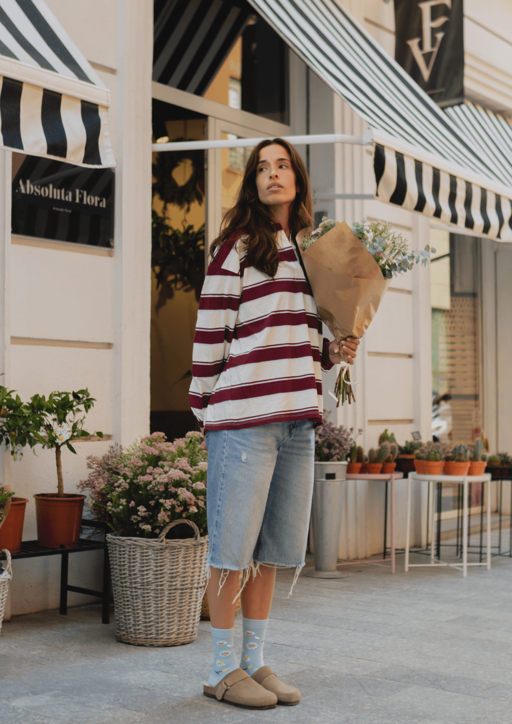 Mujer con calcetines con sandalias, camiseta a rayas y flores, en una tienda de moda casual.