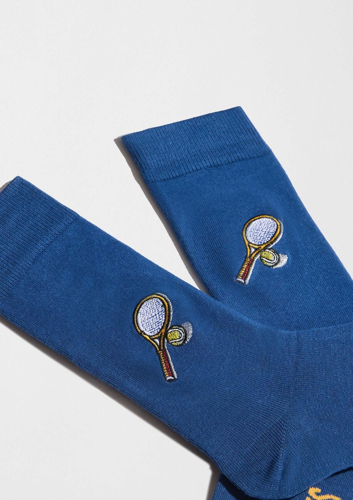 BeTennis Embroidered en calcetines azules, con bordado de raqueta y pelota de tenis en hilo blanco y rojo.