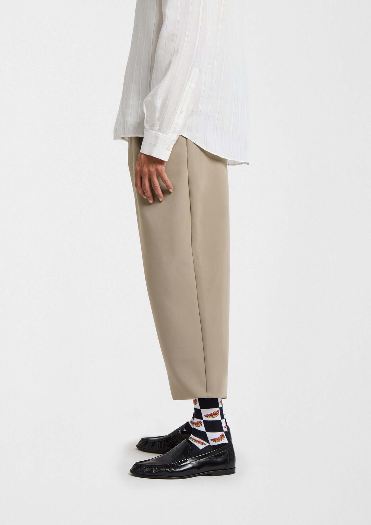 Vista lateral de un hombre con pantalones beige y calcetines BeHotDog con dibujos de hot dogs y fondo blanco.