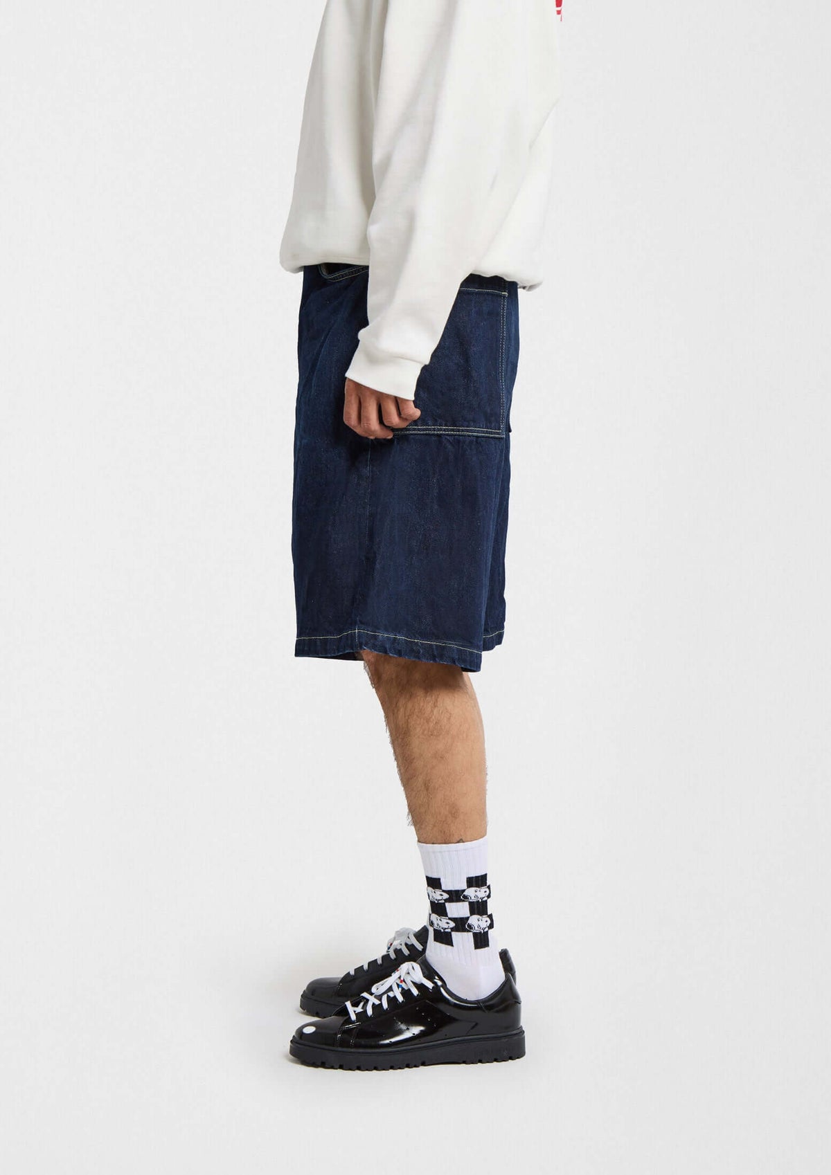 Hombre con pantalones cortos de mezclilla y calcetines altos de calcetines con dibujos sobre fondo blanco.
