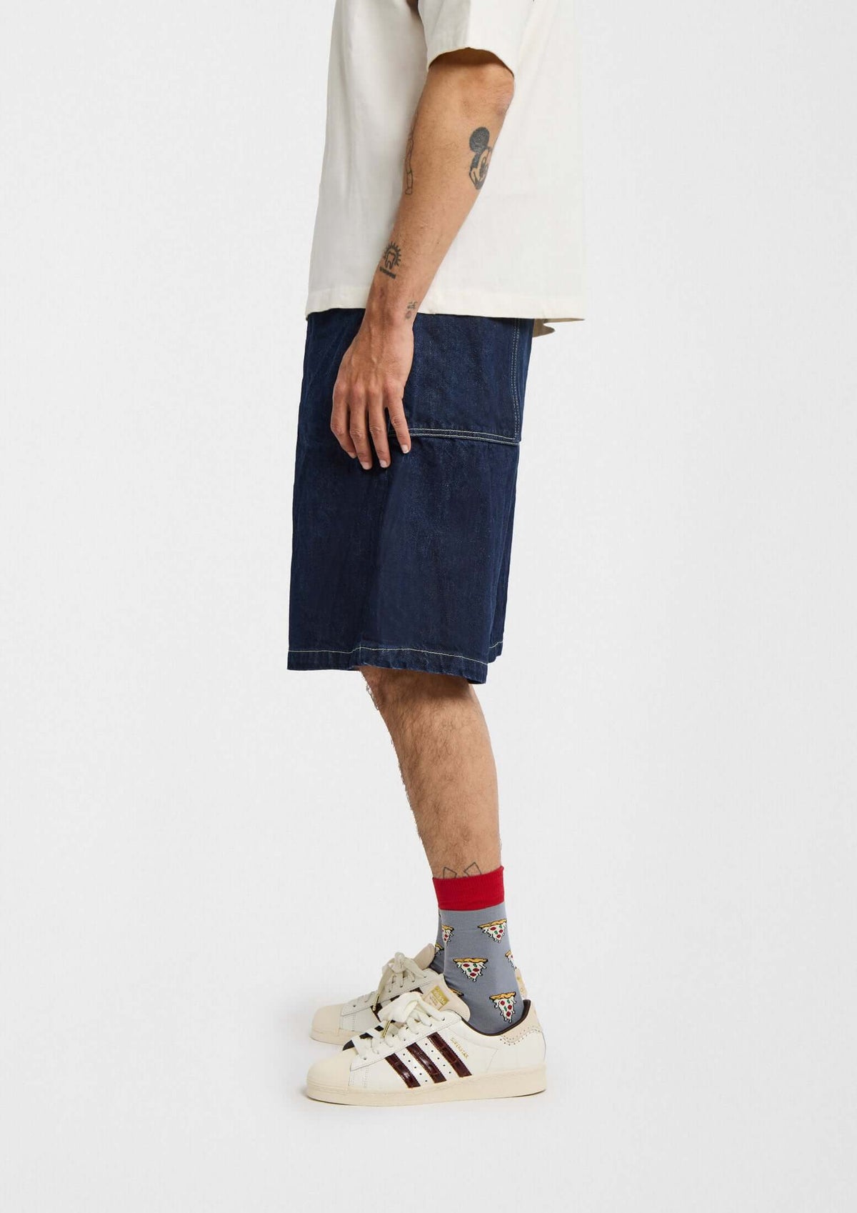 Hombre de perfil con calcetines BePizza en gris con dibujos de pizza y puntera roja, usando shorts azul marino.