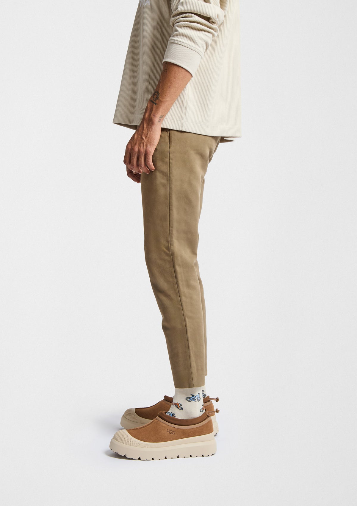 Hombre viste pantalones beige y calcetines originales BeBicycle Beige con estampado de bicicletas en tonos azul y naranja.