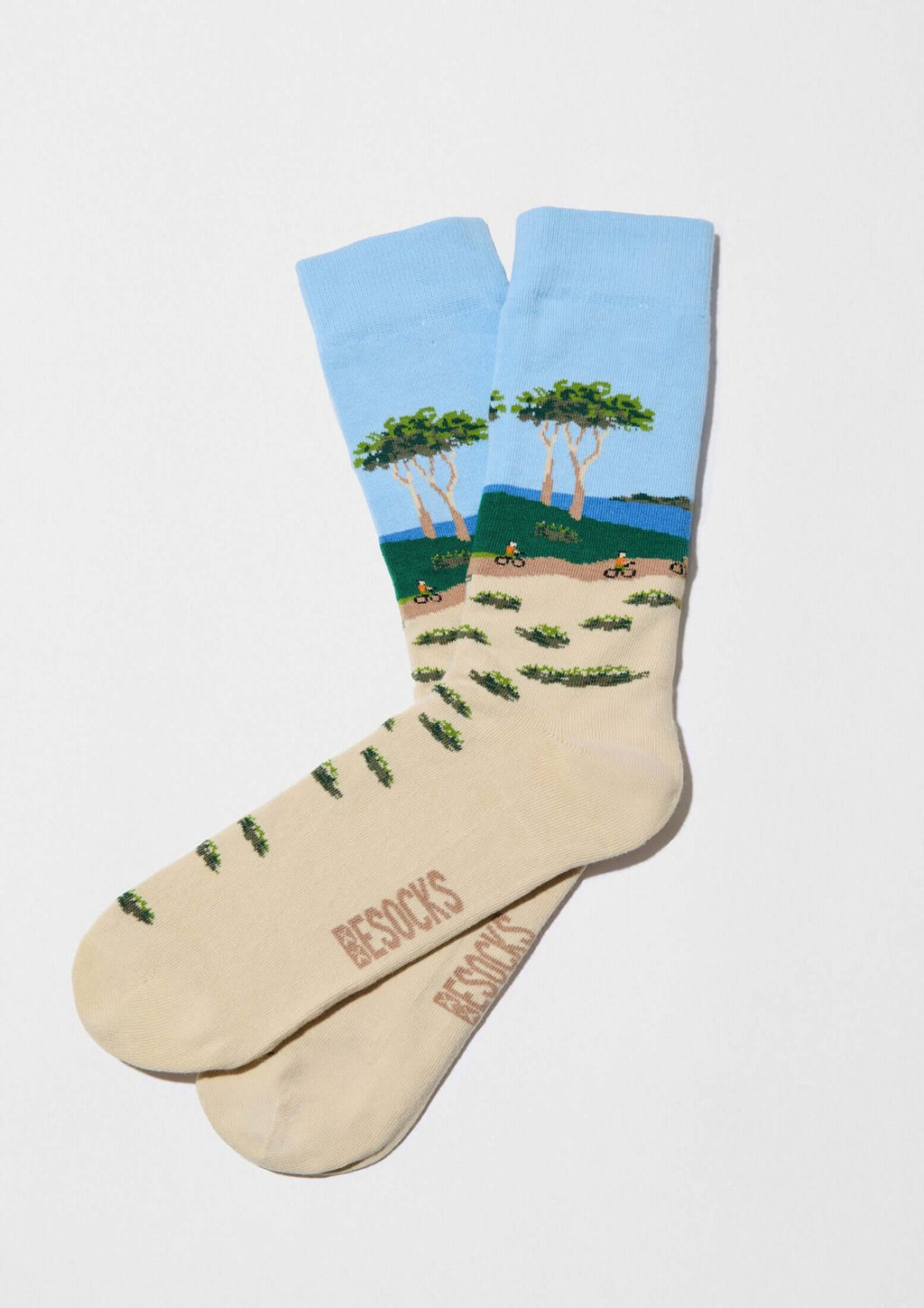 Calcetines BeLandscape de algodón orgánico en arena y azul con paisaje de árboles y ciclistas en tonos verdes y azules.