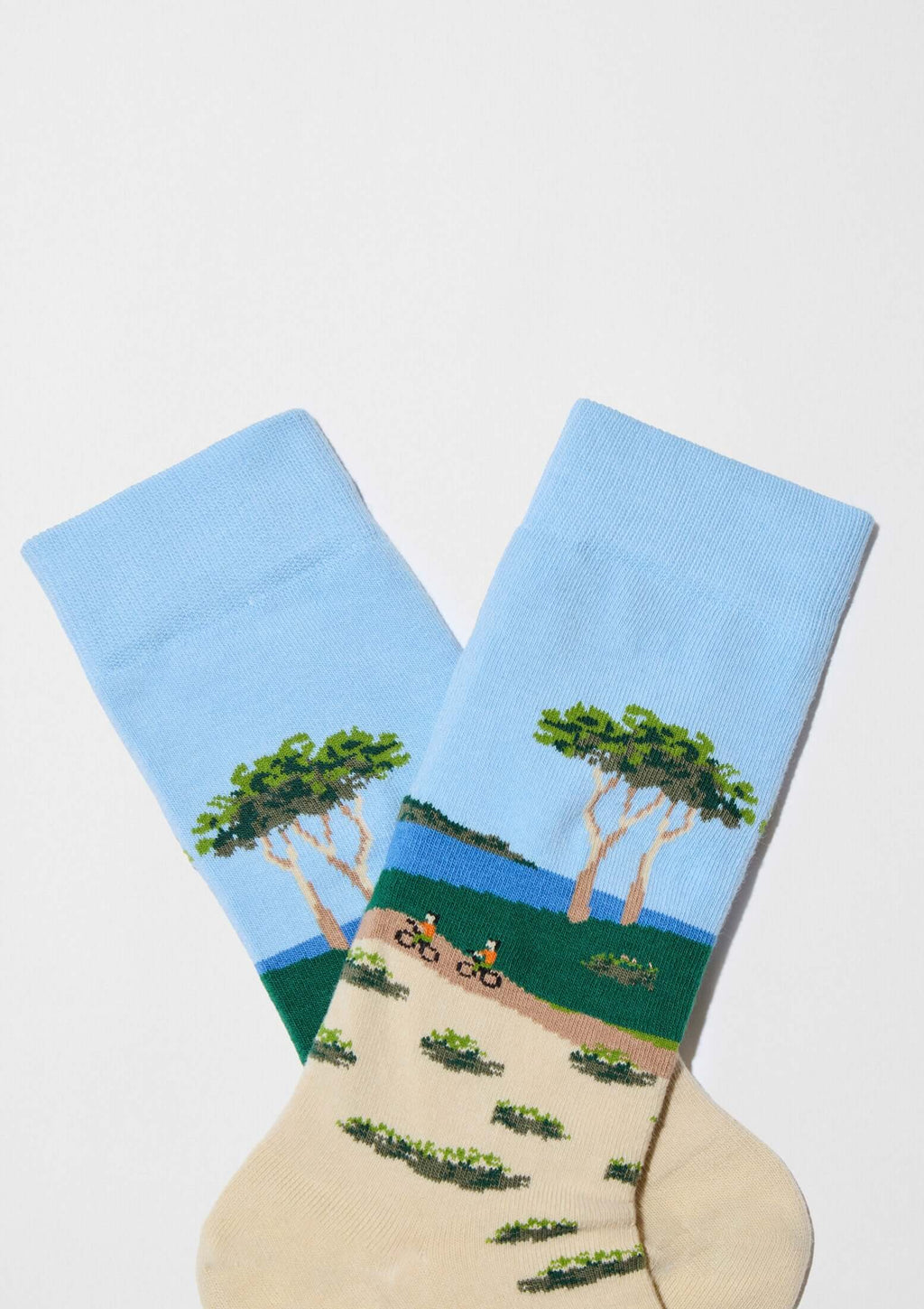 Calcetines BeLandscape de algodón orgánico en tonos arena y azul, con ciclismo y árboles sobre un paisaje natural.