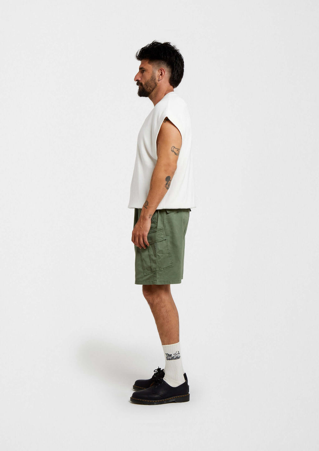 Hombre de lado con camiseta blanca y shorts verde oliva, usando calcetines BeTheGodfather Logo de media altura.