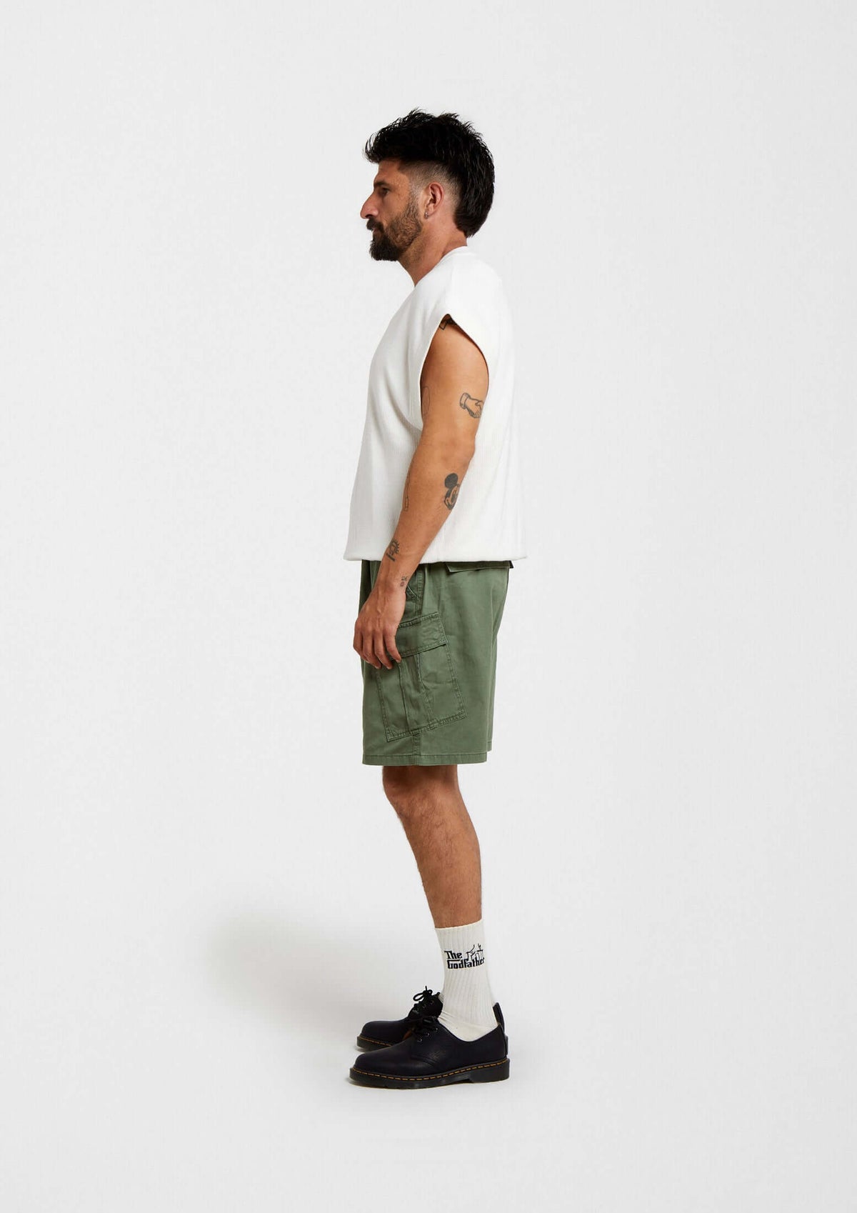 Hombre de lado con camiseta blanca y shorts verde oliva, usando calcetines BeTheGodfather Logo de media altura.