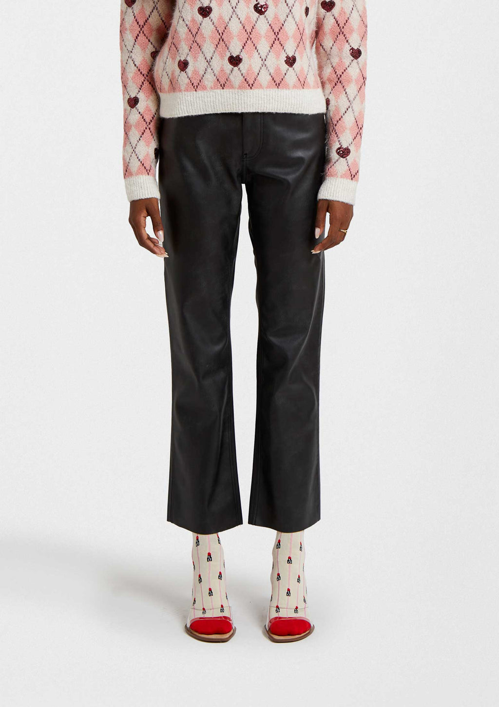 Mujer usando pantalones de cuero negro con calcetines BeEmilyinParis Lipstick Beige y suéter de corazones.