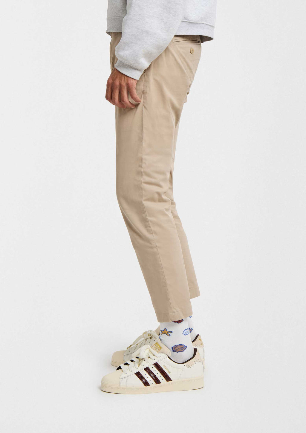 Pantalones beige ajustados con calcetines BeOcean White y zapatillas deportivas blancas en un fondo neutro.