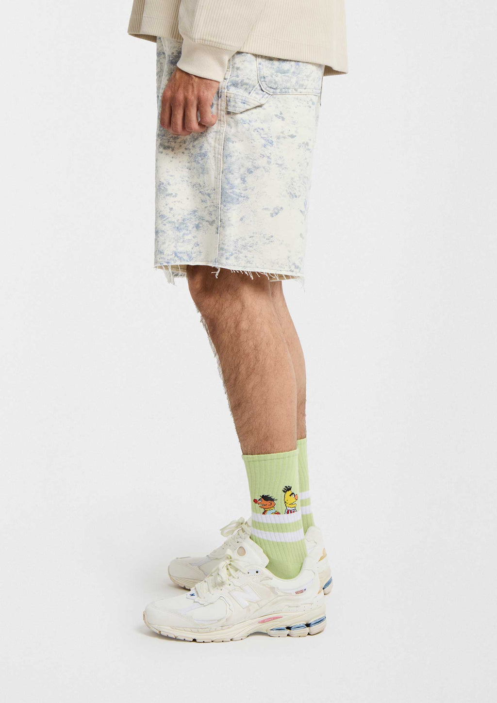 Calcetines BeSesameStreet Epi & Blas Pink con dibujos sobre fondo verde, combinados con shorts y zapatillas blancas.
