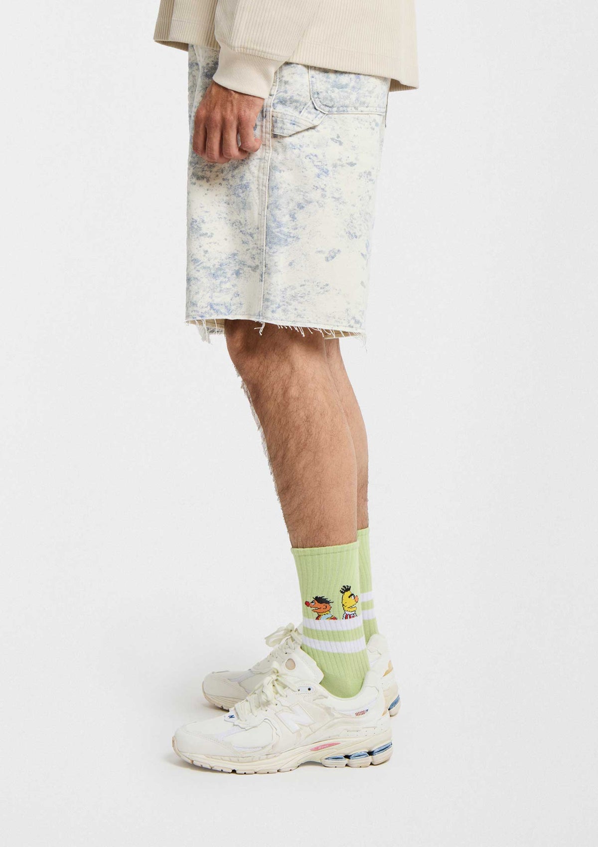 Calcetines BeSesameStreet Epi & Blas Pink con dibujos sobre fondo verde, combinados con shorts y zapatillas blancas.